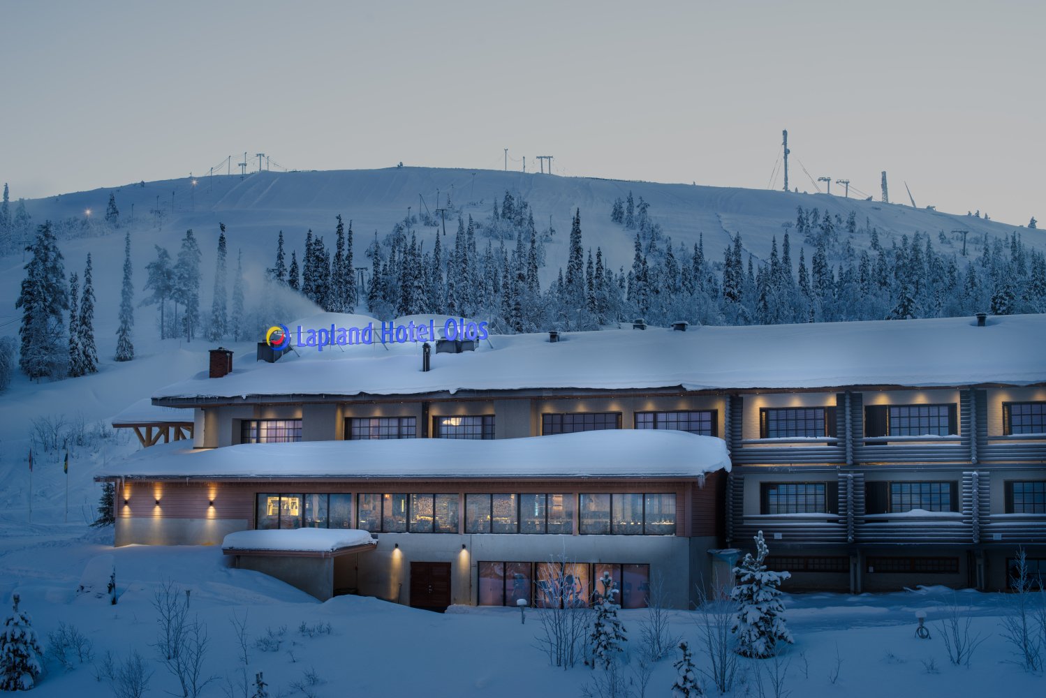 Low hotel buildings at the foot of a bare fell with ski tracks in the yard